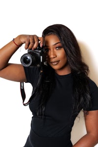 a woman holding a camera in front of a white wall